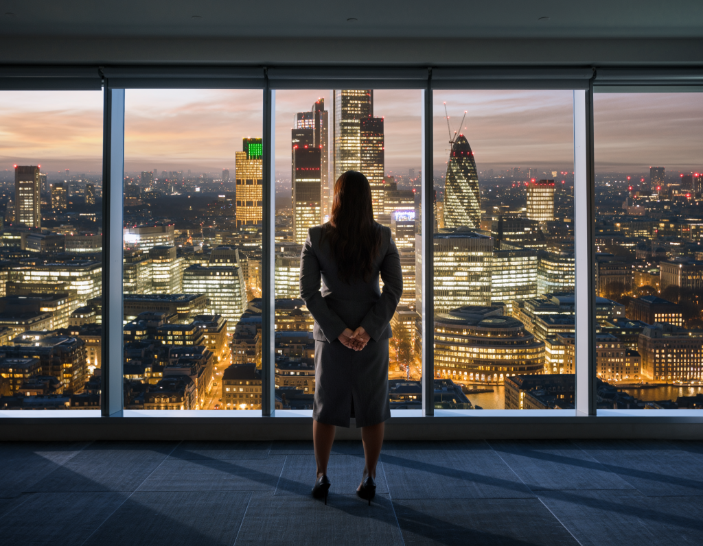 Confident UK business leader standing in a modern office, overlooking a city skyline like London, symbolizing urgency, strategy, and forward-thinking decision-making.