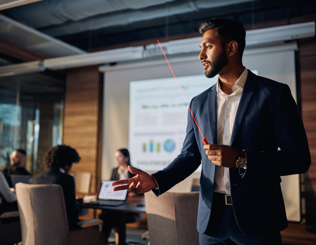 IT manager presenting quarterly metrics, conference room, PowerPoint on 4K projector, diverse team, laser pointer, modern corporate